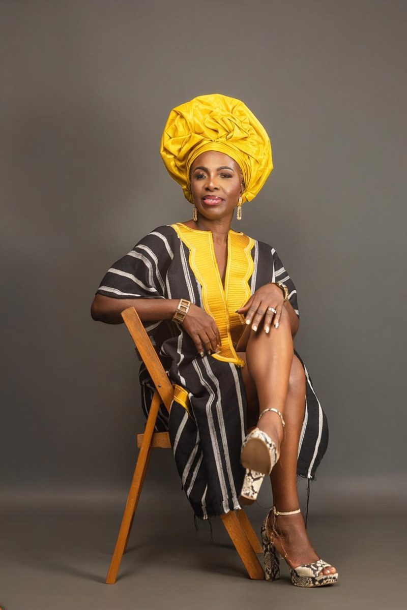 Mariama Suma-Keita, founder of MEND, seated in a gold headwrap and striped gown